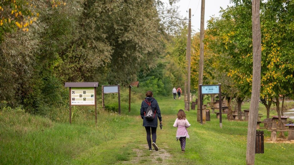 A parent and child walking on a path in a scenic nature reserve in Croatia, surrounded by lush greenery.